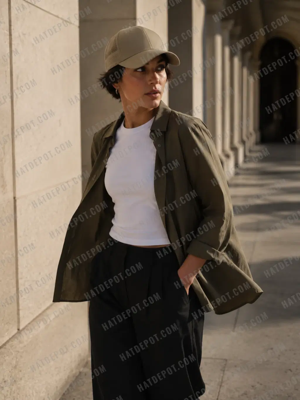 A model wearing a khaki curved-brim trucker walking through a sunlit stone arcade