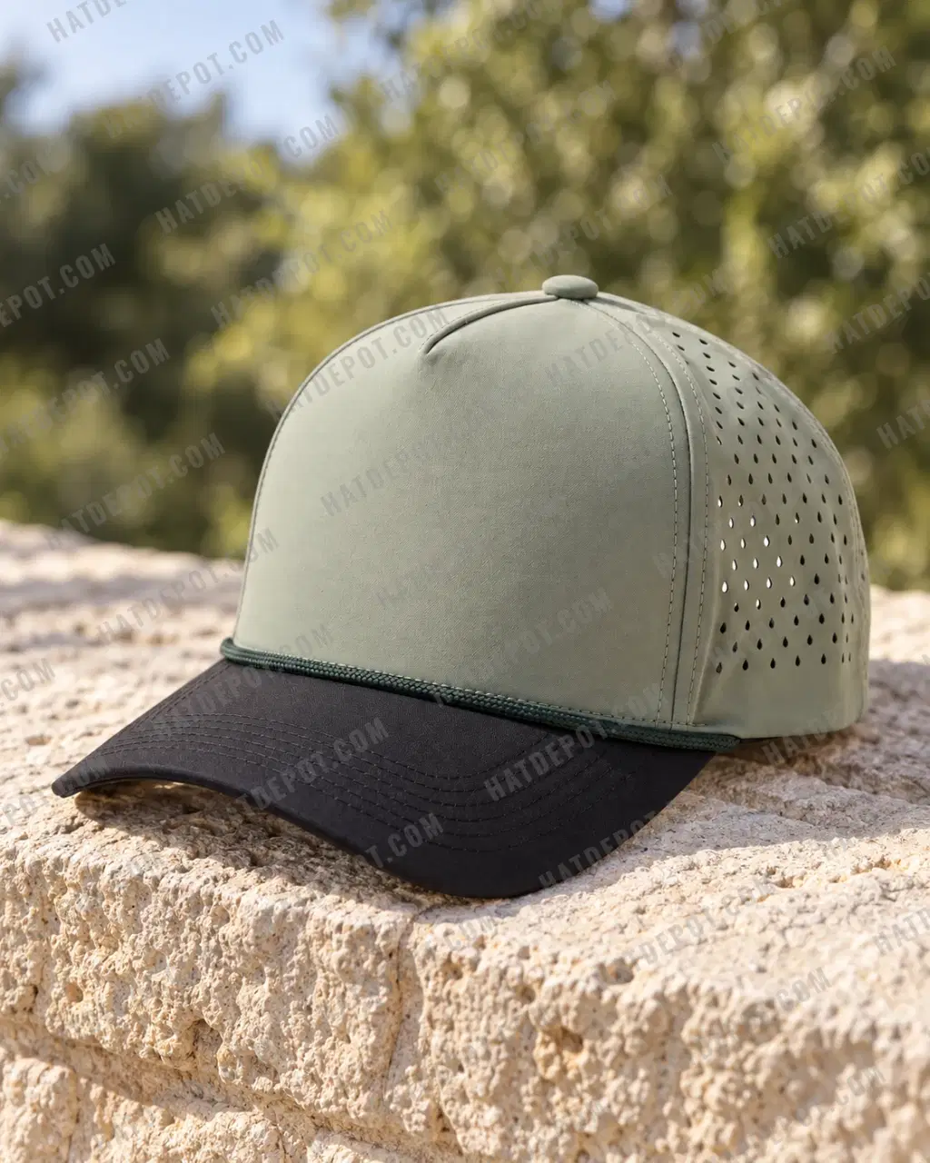 Sage / Black Curved-Brim Rope Snapback on a pale stone course wall, with raking light showing the seamless sage front, dark braided cord, curved black brim and laser-cut vents.