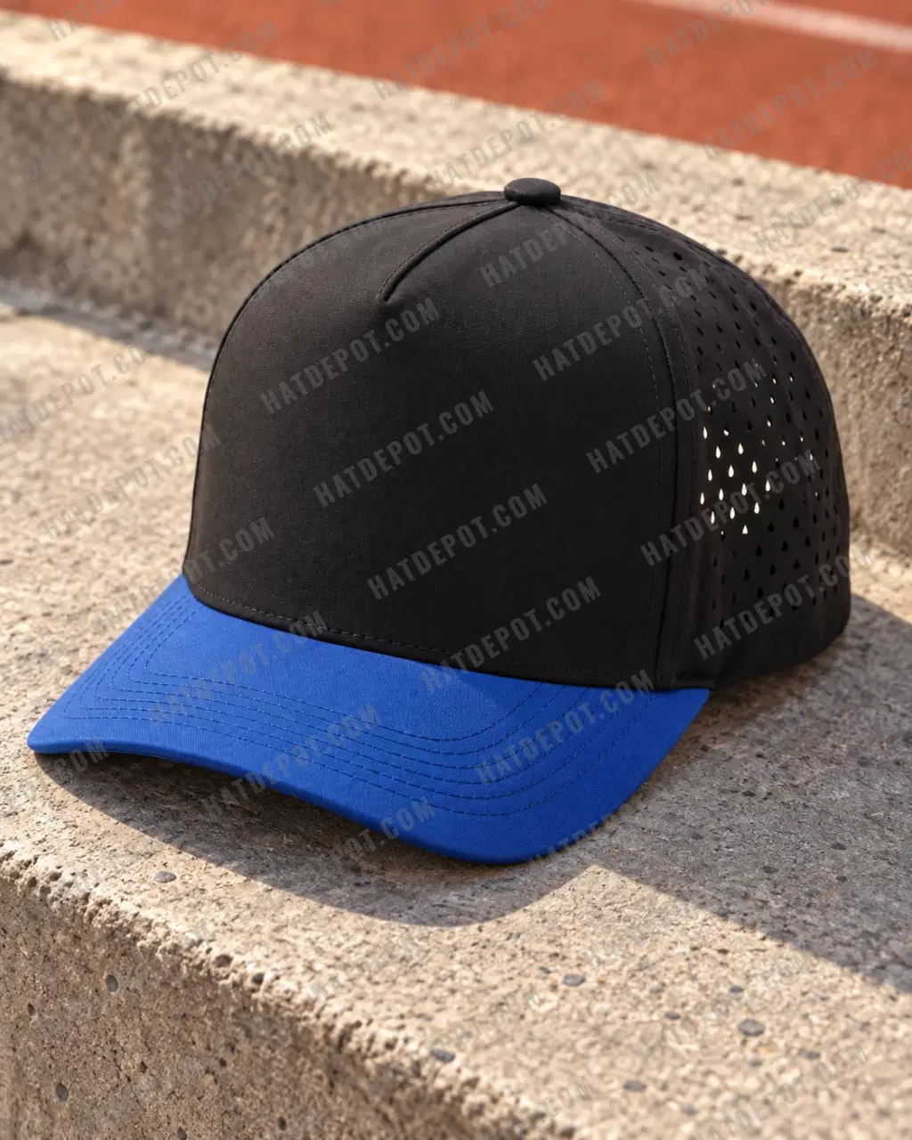 Black / Royal Five-Panel Perforated Snapback on a concrete step, with directional sunlight revealing its royal-blue curved brim, continuous black front and laser-perforated sides.