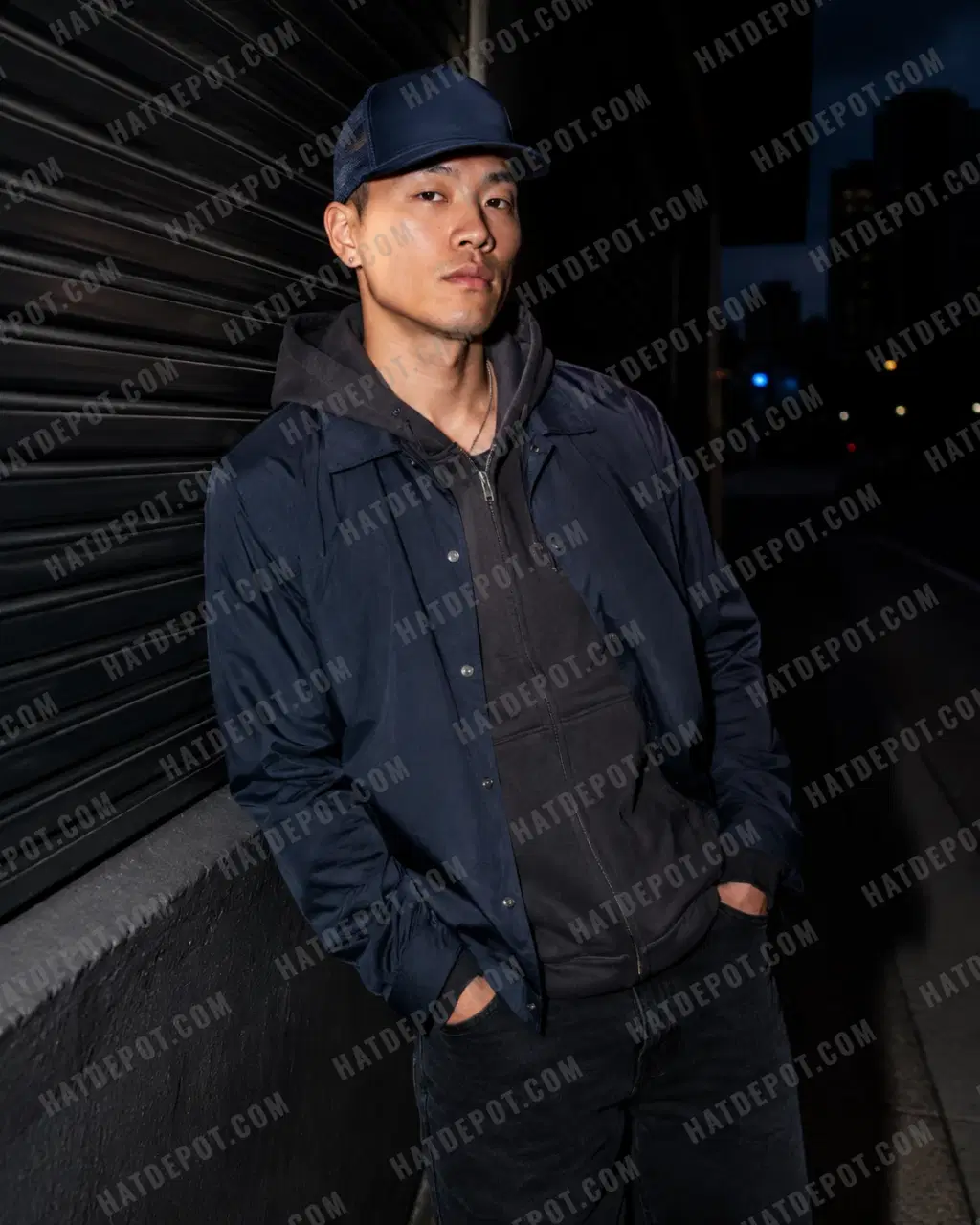 Model wearing the navy Flat Brim Trucker Snapback on a city street at night, with direct flash revealing its seamless front and flat visor.