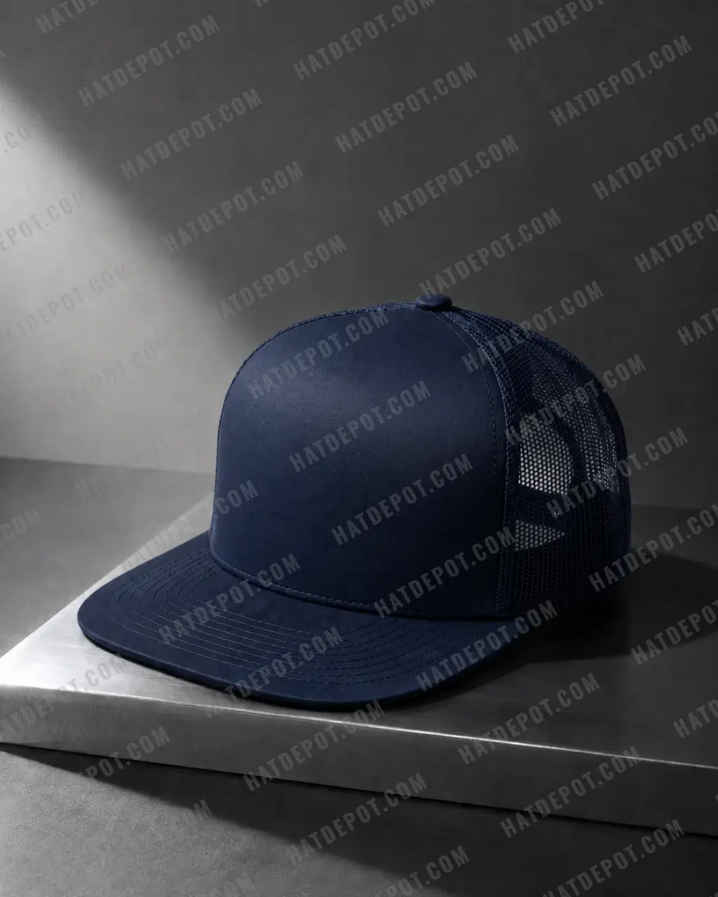 Navy Flat Brim Trucker Snapback on brushed steel, with directional light showing the flat stitched visor, smooth front panel and mesh sides.
