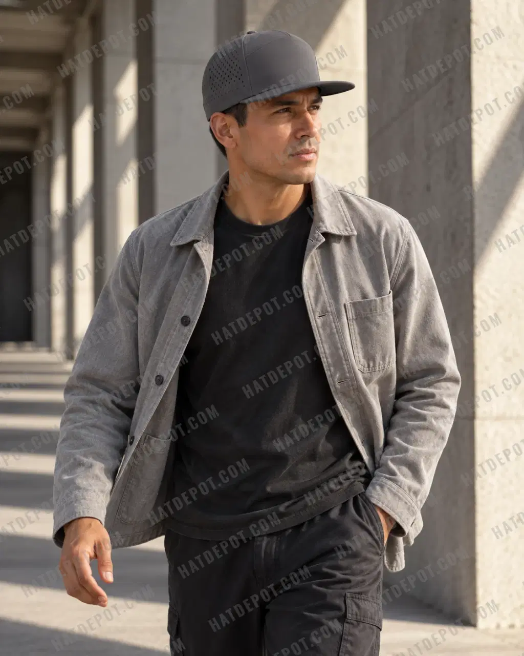 Model moving through a sunlit concrete arcade in the charcoal Seven-Panel Perforated Snapback, showing its flat visor and seamless front.