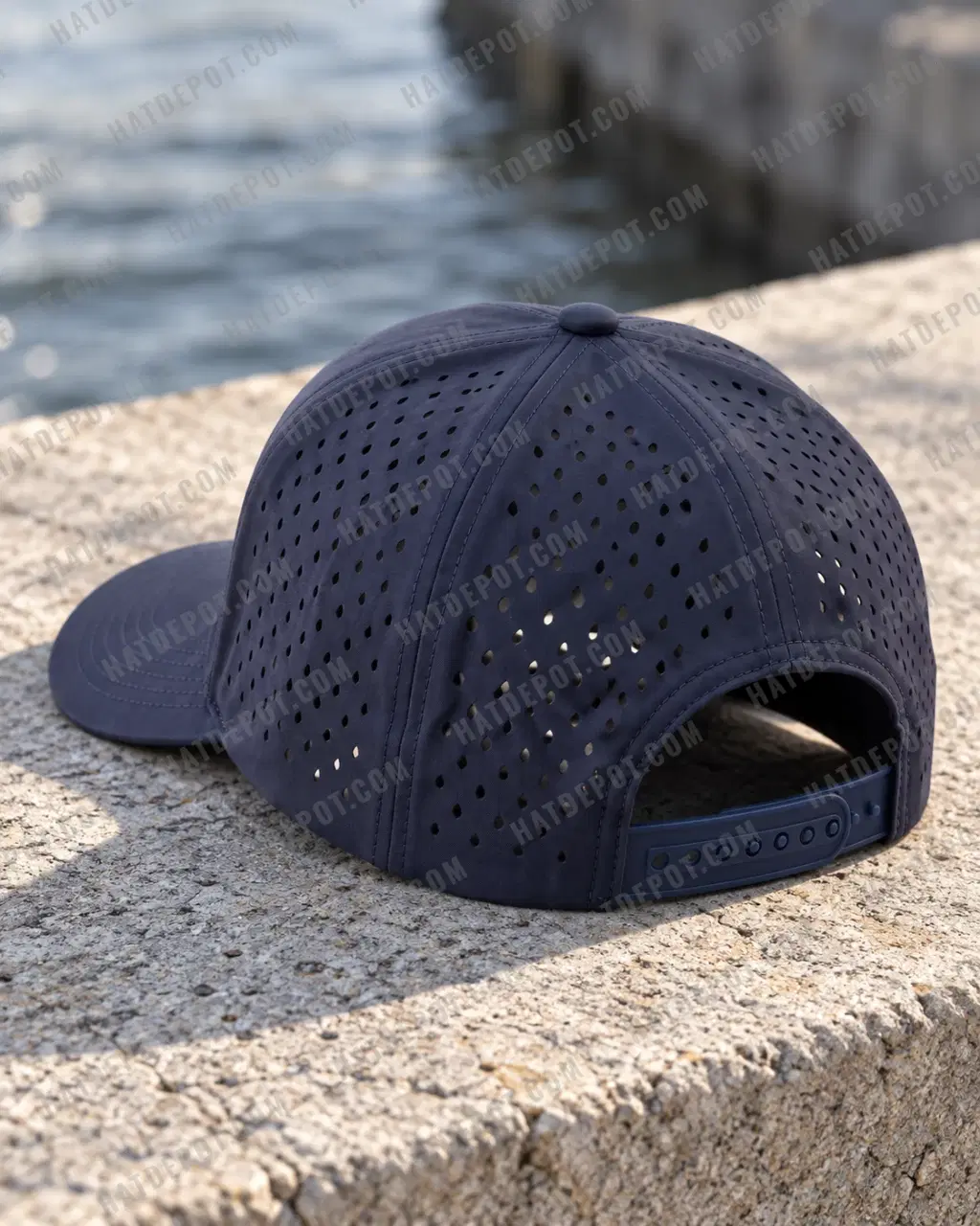 Navy Six-Panel Perforated Snapback on a concrete ledge, viewed from the rear to show its regular laser-perforation grid and matching plastic snap closure.